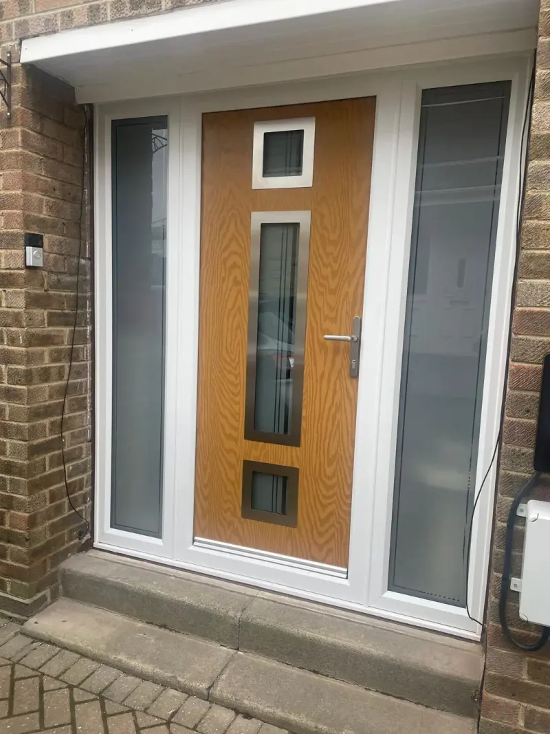 An oak-look composite door with three glazed panels in brushed-steel surrounds, a white frame, and a frosted sidelight to each side.